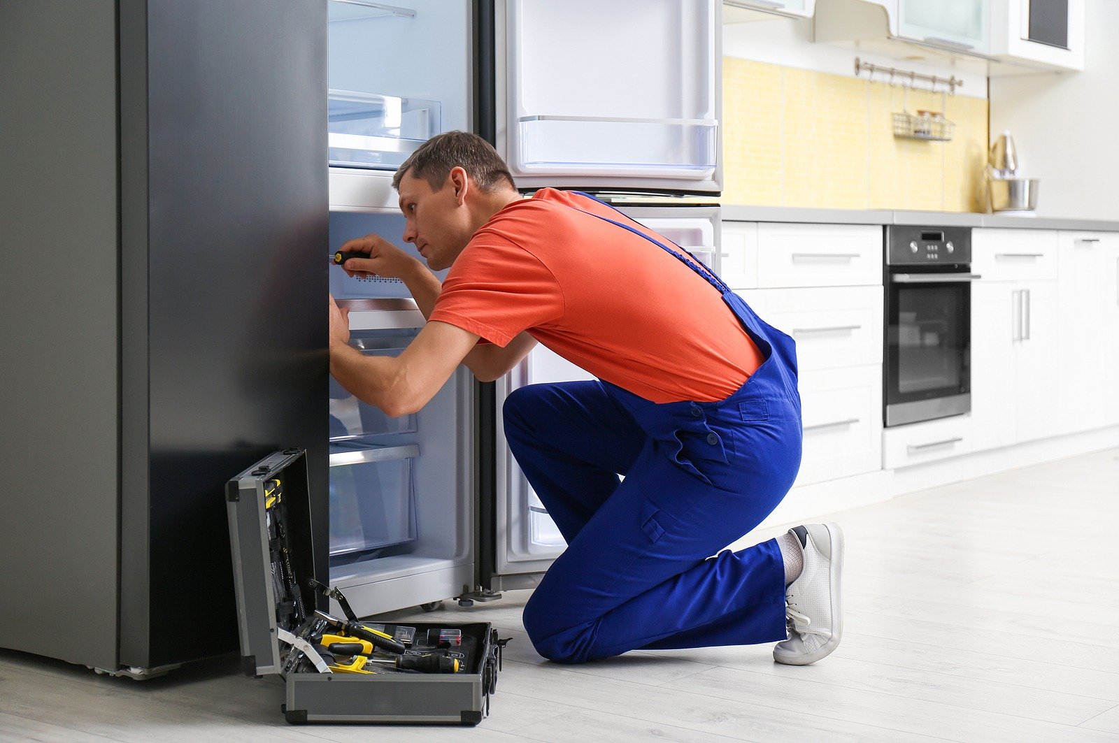 Male-Technician-With-Screwdriver-Repairing-Refrigerator-in-Kitchen